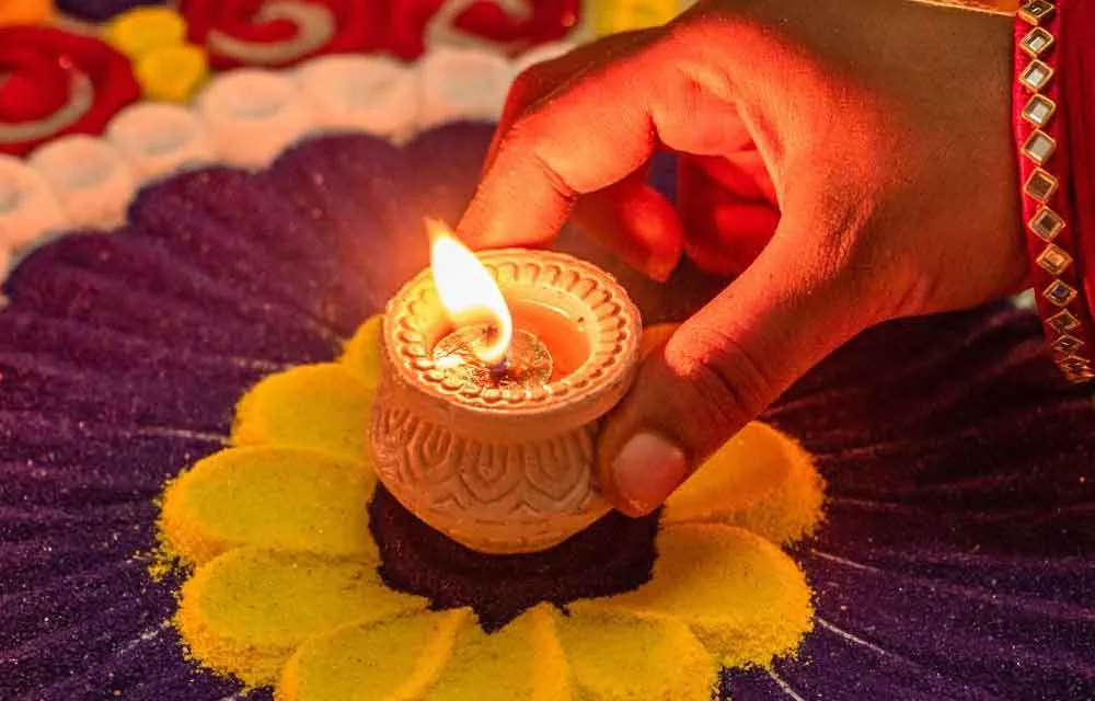 Hand placing a lit clay diya on a colourful rangoli